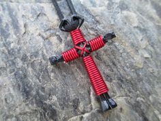 a close up of a red and black metal cross on a stone surface with rocks in the background