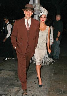 a man and woman walking down the street at night wearing brown suits with fringes on them