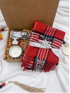 an open box containing a candle, teapot and other items on a white blanket