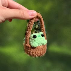 a hand holding a small crocheted bag with a frog face on it's handle