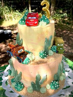 a three tiered cake with cars and trees on the top is decorated in yellow frosting