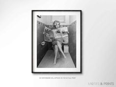 a black and white photo of a woman sitting on a toilet reading a newspaper in the bathroom