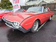 an old red car is parked in the parking lot next to other classic cars on display