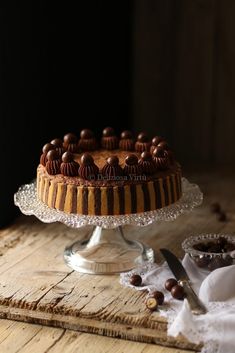 a cake sitting on top of a wooden table next to a knife and bowl filled with nuts