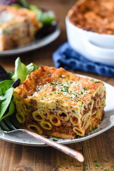 a slice of lasagna on a white plate with a fork and salad in the background