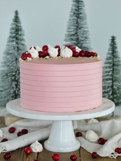 a pink frosted cake with cranberries and white icing on a wooden table