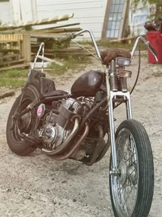 a motorcycle parked on the side of a dirt road next to a building and fence