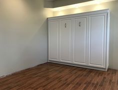 an empty room with white cabinets and hard wood floors