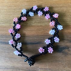 a beaded bracelet with pink and white flowers on black beads is sitting on a wooden surface