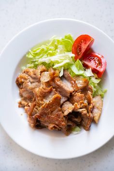 a white plate topped with meat, lettuce and tomatoes