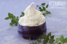 a purple bowl filled with whipped cream on top of a blue table cloth next to green leaves