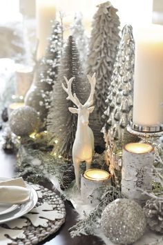 a christmas table setting with candles, silver and white decorations and deer figurines