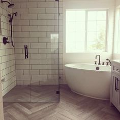 a white bath tub sitting next to a window in a bathroom on top of a wooden floor