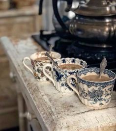 three coffee mugs sitting on top of a wooden table next to a tea pot