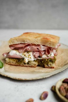 a sandwich with meat, cheese and pesto on it sitting on a plate next to nuts