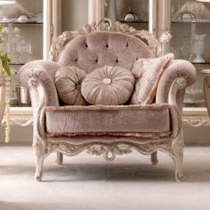 a chair with pillows on it sitting in front of a glass case and some shelves