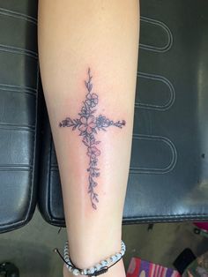 a cross tattoo on the leg with flowers and leaves around it, as well as a beaded bracelet