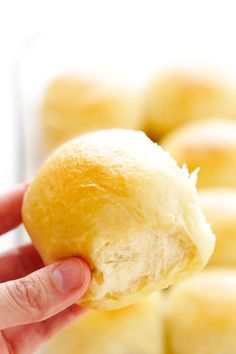 a hand holding a piece of bread in front of some other rolls on a plate