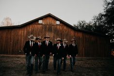 four men in suits and cowboy hats standing next to a barn