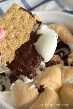 someone is dipping some ice cream on top of cookies and marshmallows in a bowl