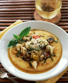 a white bowl filled with soup on top of a wooden table next to a glass of wine