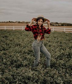 a woman standing in a field holding her hat over her head and smiling at the camera