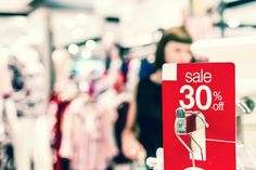 a red sale sign sitting on top of a white shelf next to clothes in a store