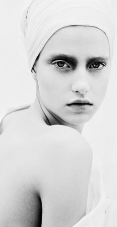 a black and white photo of a woman with a towel on her head looking at the camera