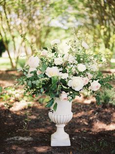 a vase filled with white flowers sitting on top of a lush green forest covered ground