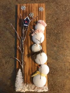 three snowmen are sitting on a wooden board with some branches and decorations around them