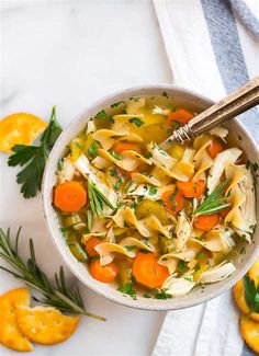 a bowl of chicken noodle soup with carrots and parsley on the side