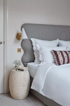 a bed with white sheets and pillows in a bedroom next to a door that has a striped headboard