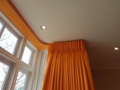 an orange curtain hanging from the ceiling in front of two large windows with white trim