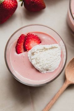 two strawberries sit on top of a bowl of yogurt next to some spoons