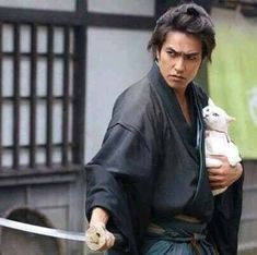 a man holding a stuffed animal in his right hand while walking down a street next to a building