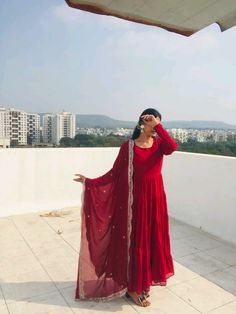 a woman in a red dress is standing on a roof with her hands behind her head