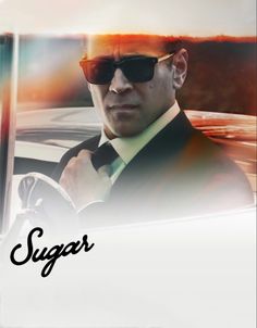 a man wearing sunglasses and a suit in front of a car with the word sugar on it