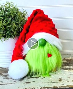 a green stuffed animal wearing a santa hat next to a potted plant