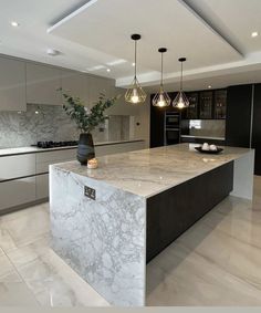 a large kitchen with marble counter tops and black cabinets, along with pendant lights hanging from the ceiling