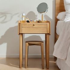 a small wooden table with a mirror on top of it next to a bed and pillows