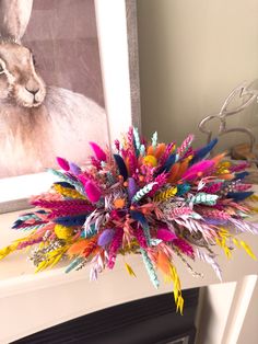 a bouquet of colorful feathers sitting on top of a mantle next to a framed photo