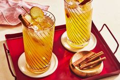 two glasses filled with drinks sitting on top of a red tray next to cinnamon sticks