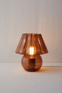 a brown glass table lamp with a light on it's side and a white wall in the background