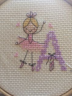 a close up of a cross stitch pattern with a girl holding a pink letter on it