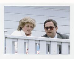 a man and woman sitting on the back of a white fence next to each other