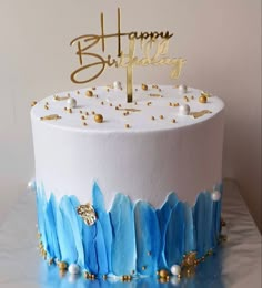 a white and blue birthday cake with gold decorations on the top that says happy birthday