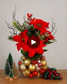 a vase filled with red flowers and ornaments on top of a wooden table next to christmas trees