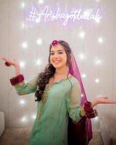 a woman in a green dress posing for the camera with her hands out and lights behind her