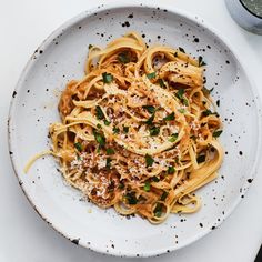 a white plate topped with pasta covered in parmesan cheese and green onion sprinkles