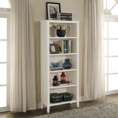 a white book shelf with books and vases on top of it in a living room